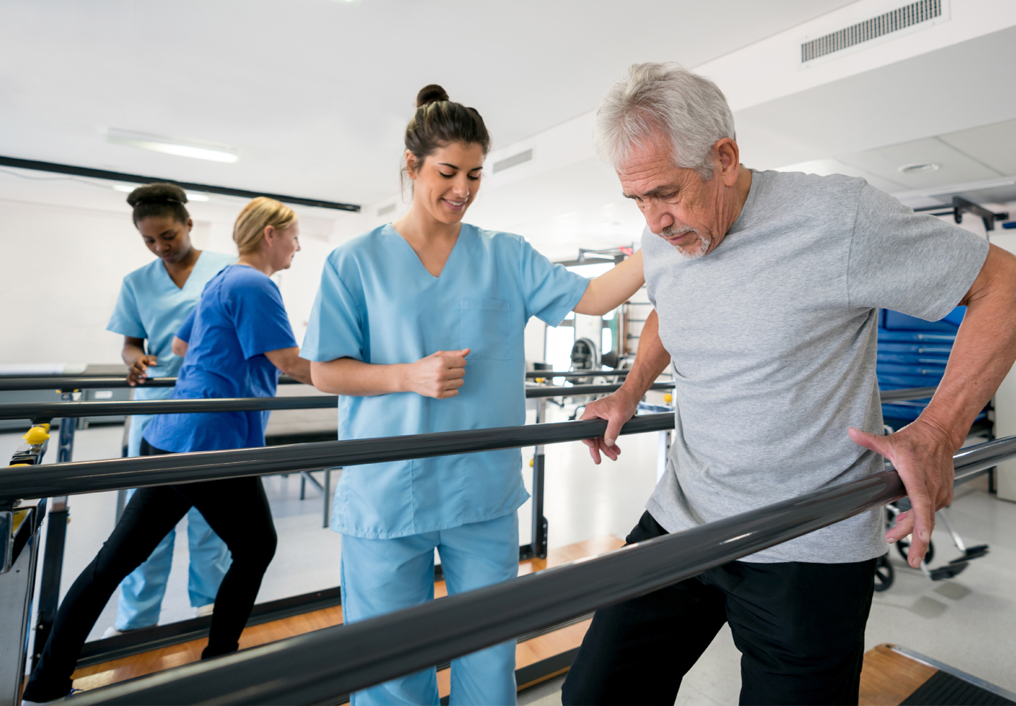 Team of physiotherapist helping senior patients walk between parallel bart